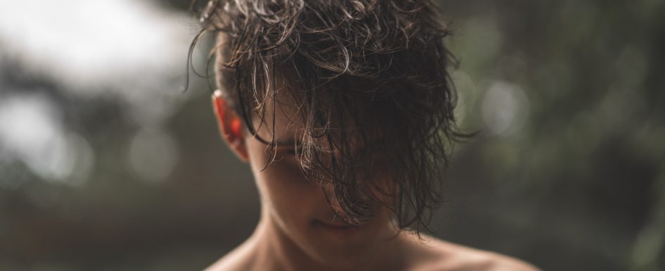 A man looks down so his hair covers his face. Photo.